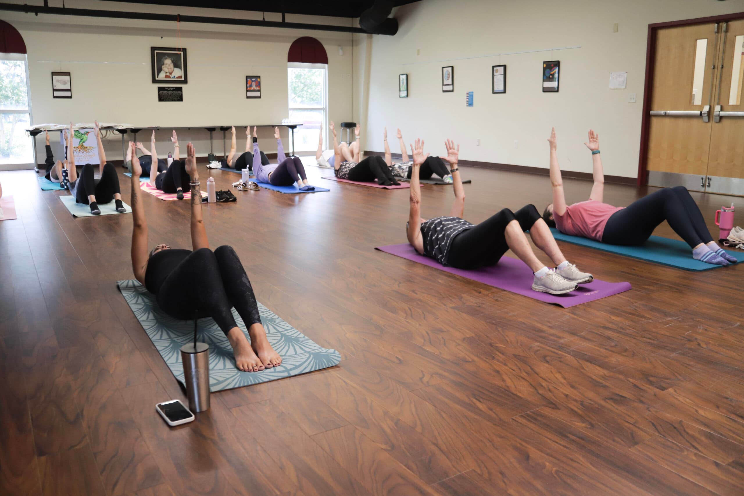 A Rooted in Strength Pilates community mat class lying on mats with arms reaching overhead
