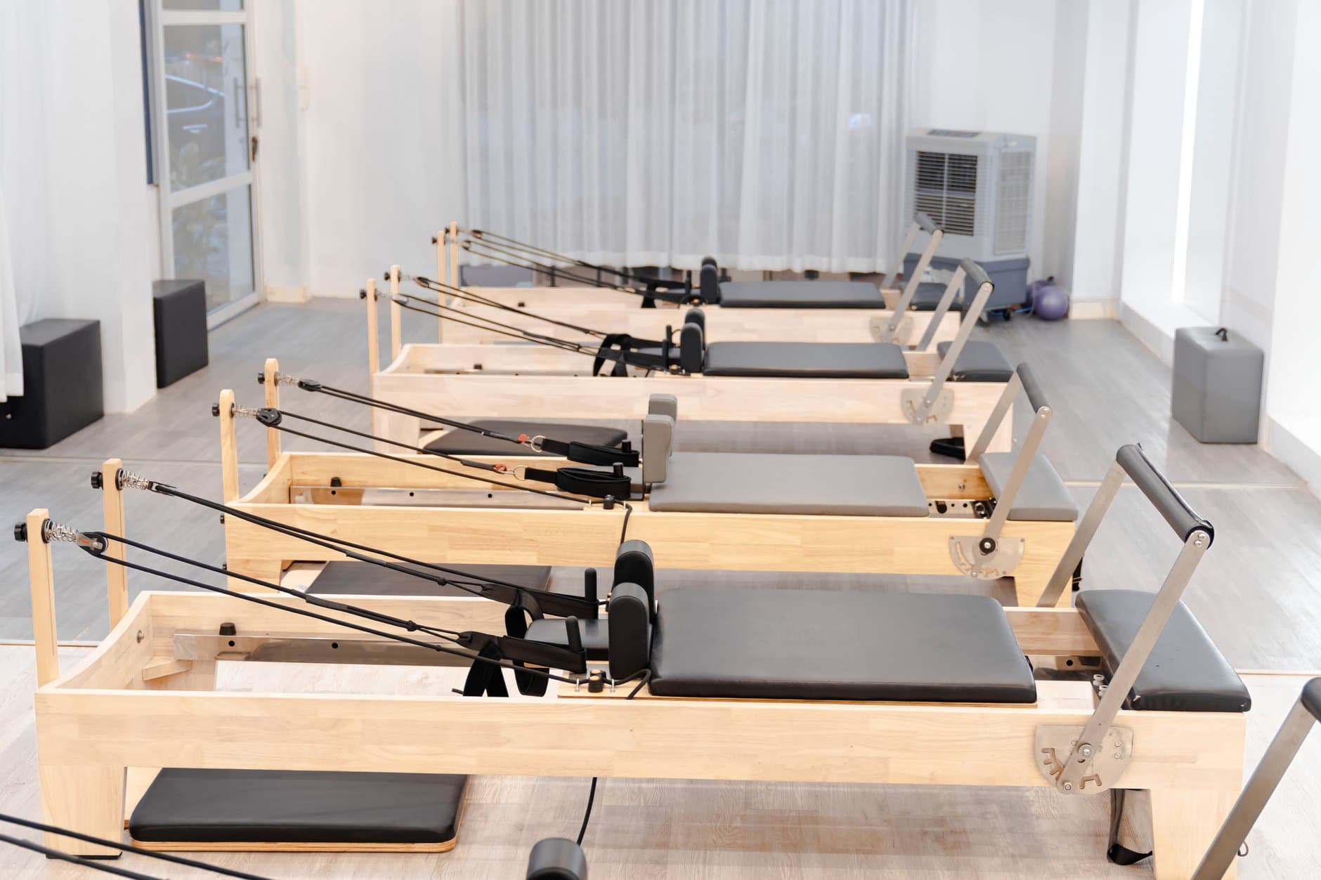 A row of light-wood Pilates reformers in a bright studio